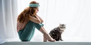 A woman sitting on a window sill with a cat.