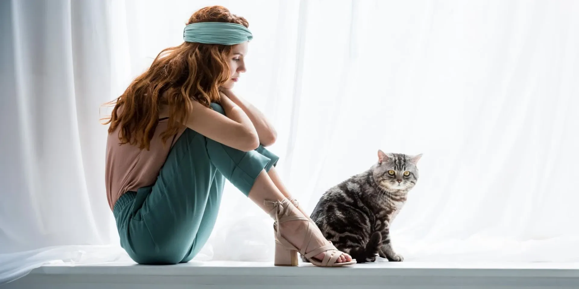 A woman sitting on a window sill with a cat.